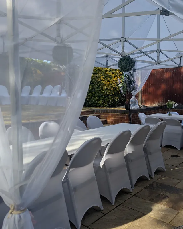 Inside a dressed garden gazebo: covered chairs, laid tables and tied drapes