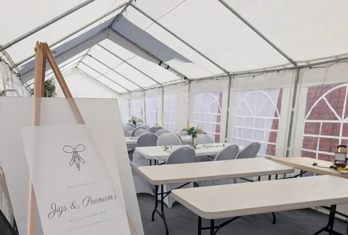 A lined marquee set out with tables for a housewarming party