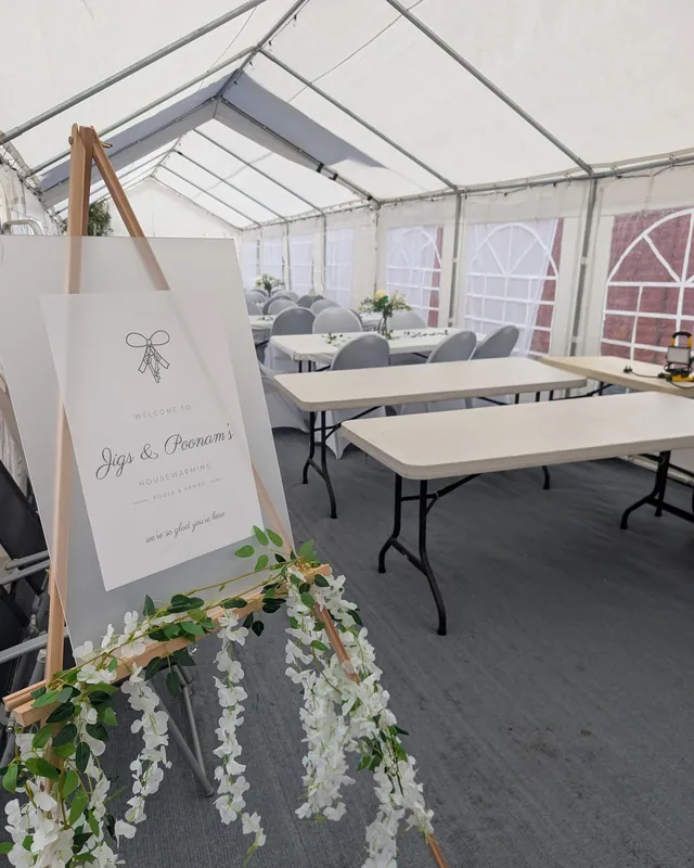 A lined marquee laid out with tables and covered chairs for a housewarming party