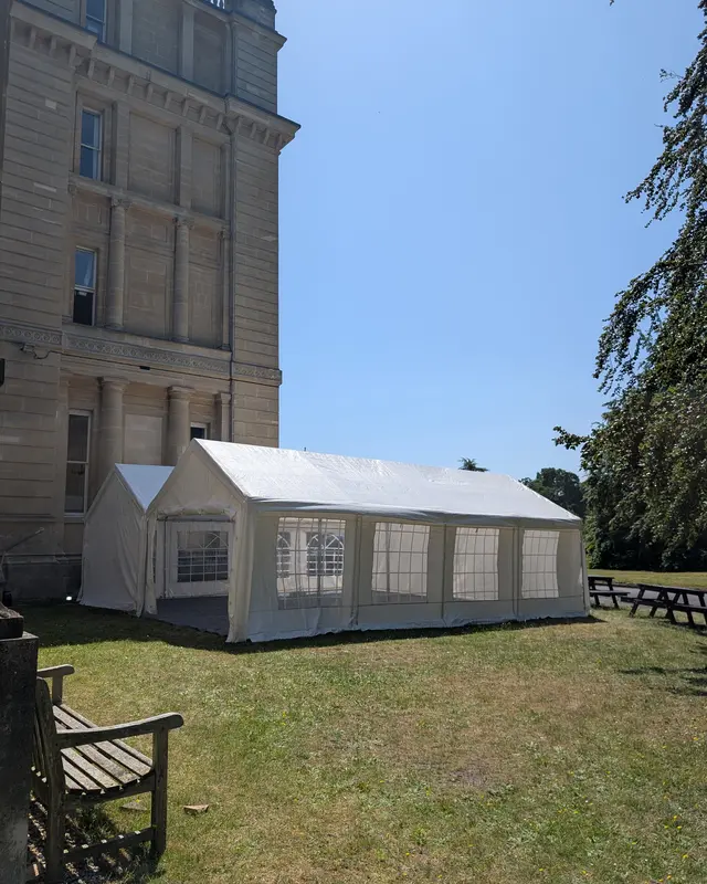 Linked marquees with full sides and window panels on the lawn of a period stone building, set for a corporate event